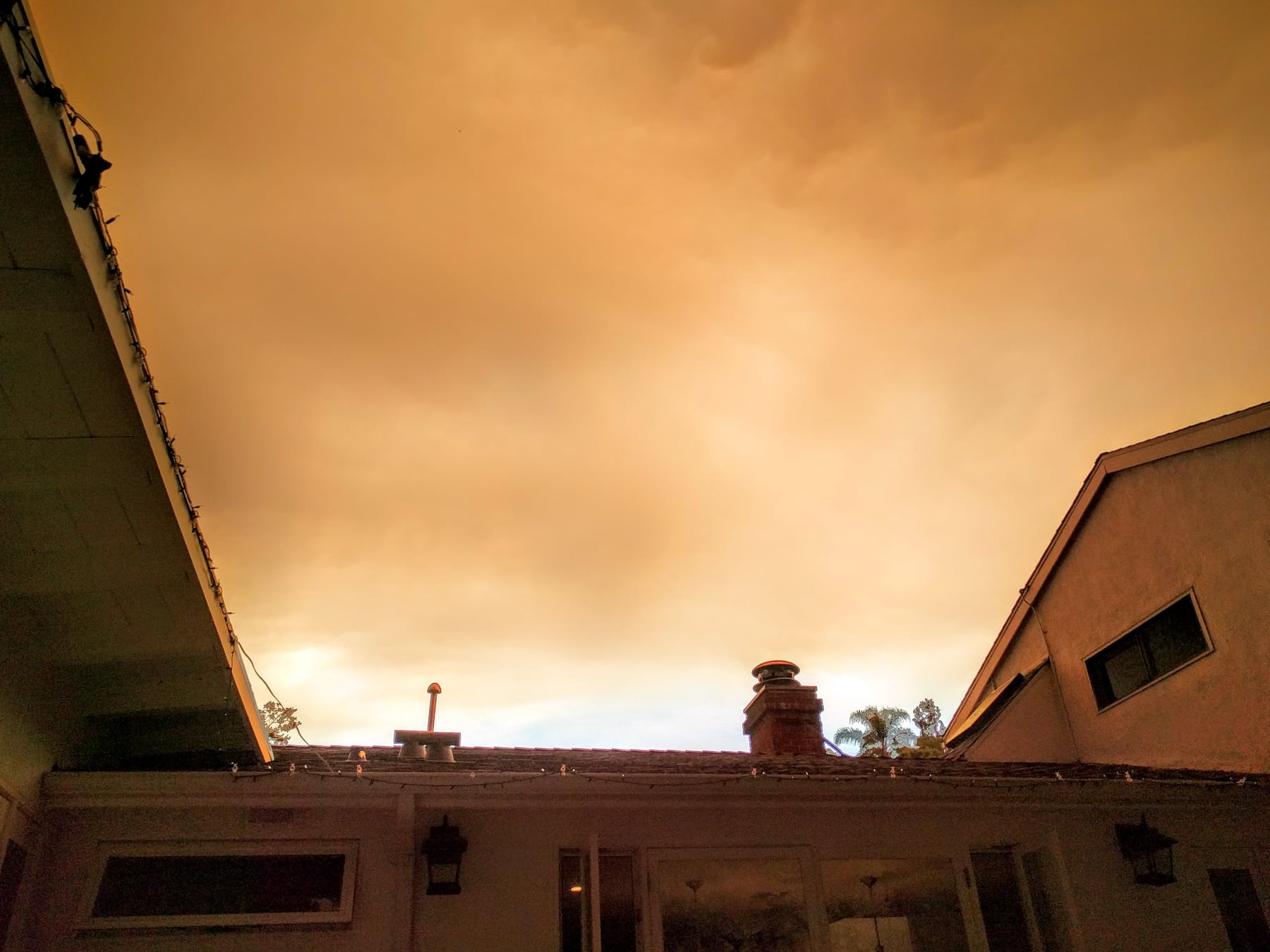 Smoke-hazed orange sky above suburban rooftops and silhouetted pines