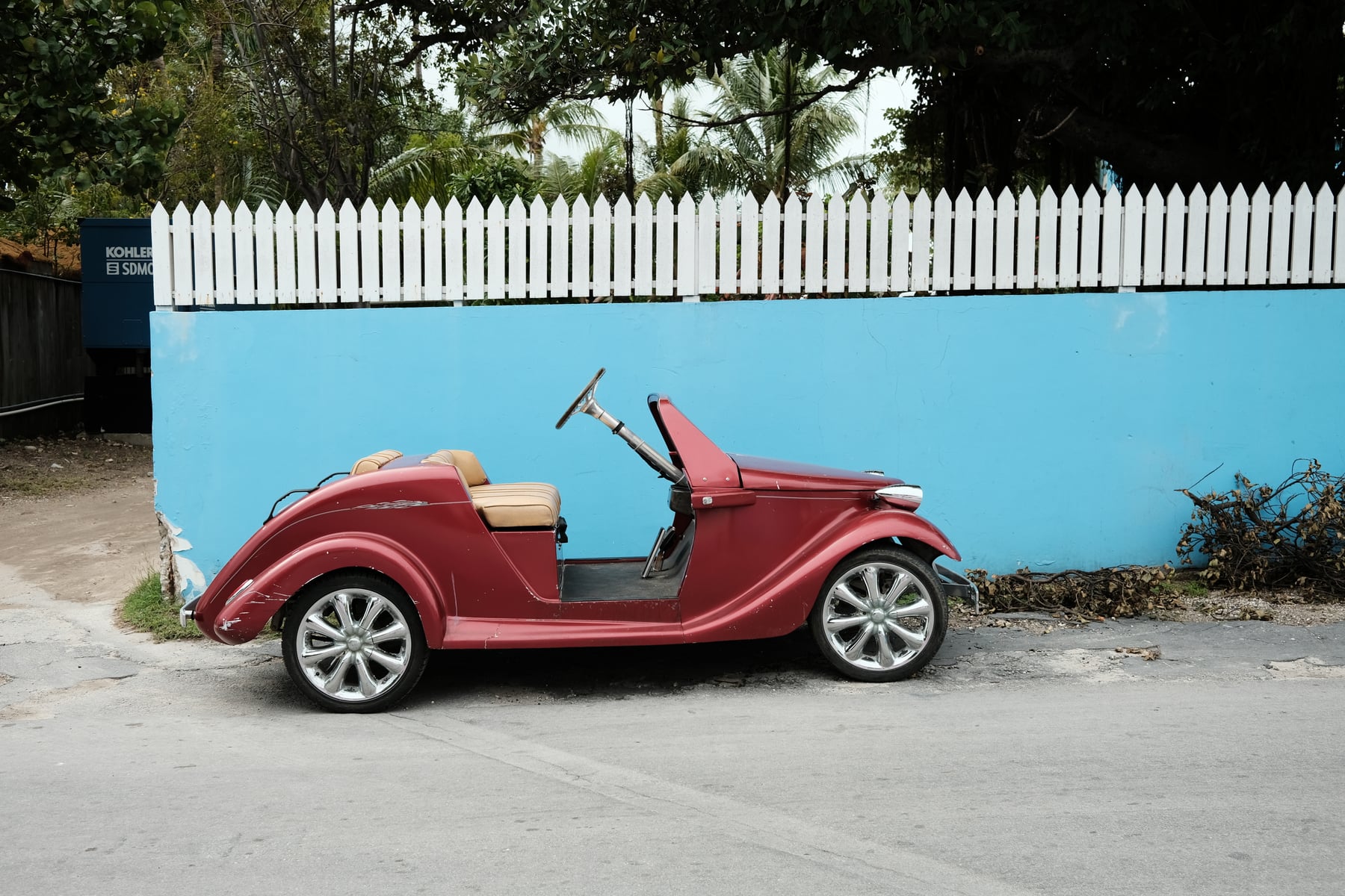 Vintage-style red golf cart parked against a bright turquoise wall