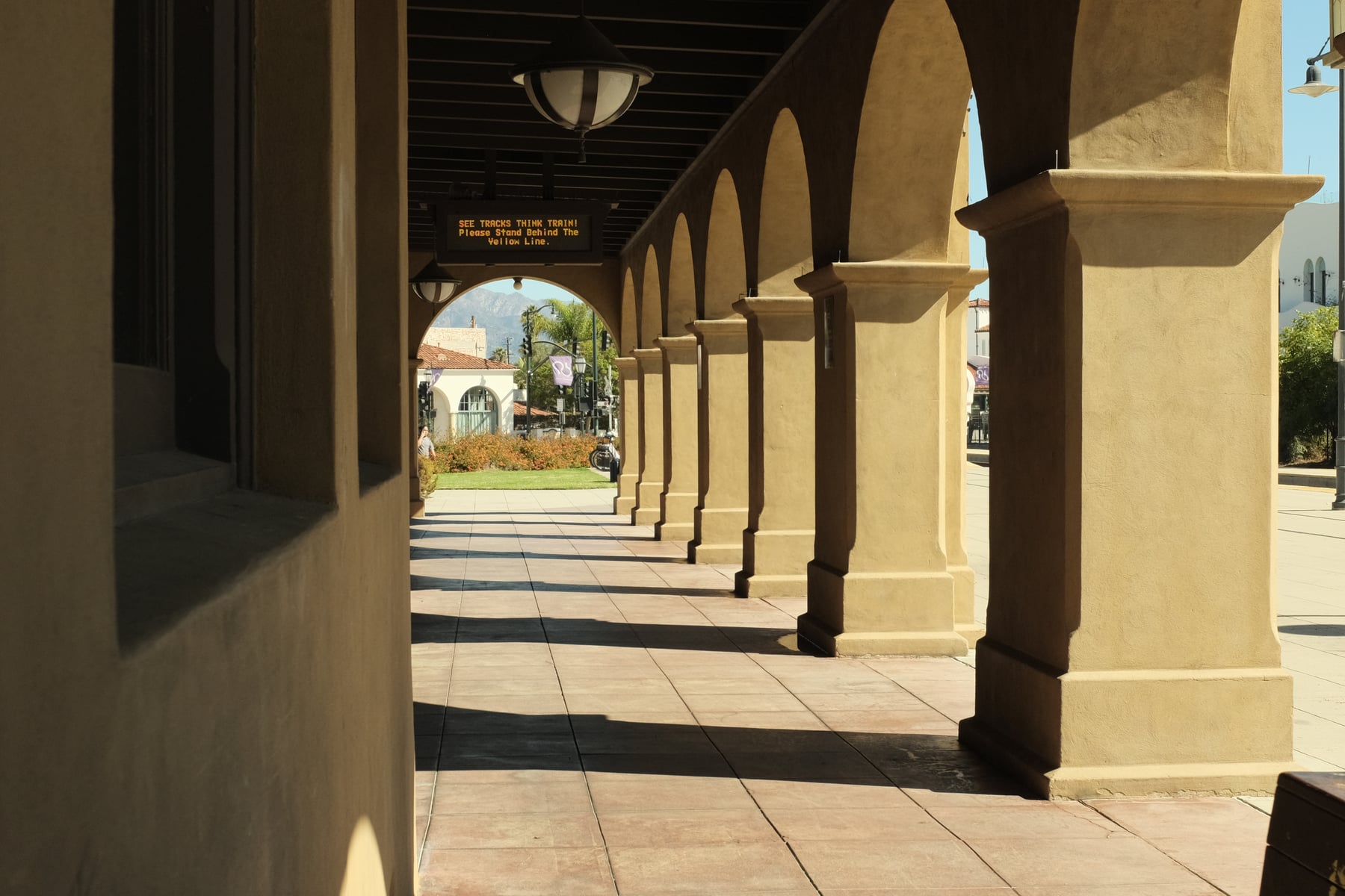 Spanish mission covered walkway, repeating arched columns casting diagonal shadows