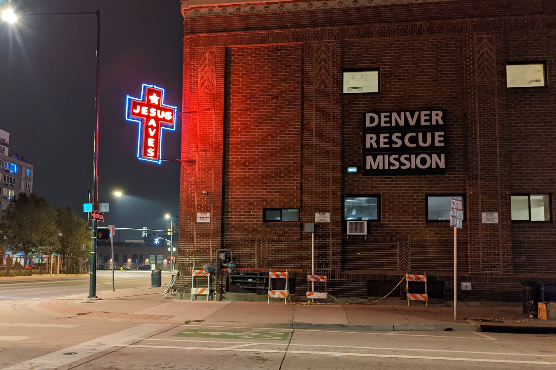Denver Rescue Mission brick building at night with glowing neon Jesus Saves cross