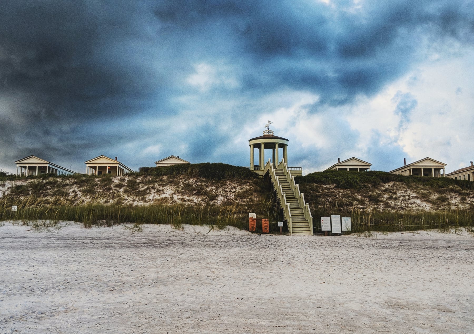 White beach pavilion on sand dunes against a bruised storm sky